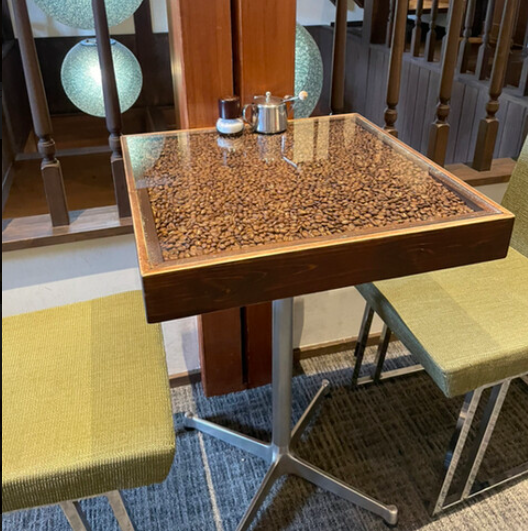 透明の天板にコーヒー豆がぎっしりと詰められているテーブル
